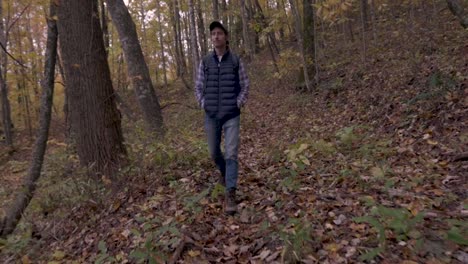 Man-hiking-towards-the-camera-in-the-fall-with-his-hands-in-his-vest-pockets