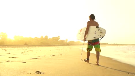 Surfer-walking-out-of-the-water-after-session-at-sunset