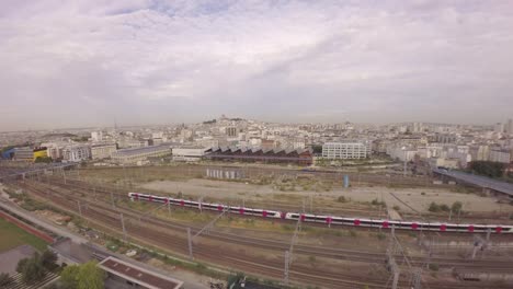 Paris,-10th-arrondissement---Aerial-view-of-TGV-high-speed-train-passing-at-Gare-du-Nord-with-Halle-Pajol-and-city-skyline-in-background