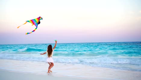 Adorable-niña-con-volar-la-cometa-en-la-playa-tropical.-Juego-de-niños-en-la-orilla-del-mar-con-hermosa-puesta-de-sol