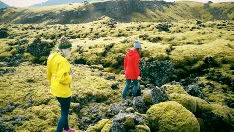 Copter-flying-around-two-woman-on-lava-field-in-Iceland.-Tourists-with-camera-walking-on-the-nature-and-taking-photos