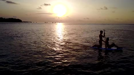 v04076-Aerial-flying-drone-view-of-Maldives-white-sandy-beach-2-people-young-couple-man-woman-paddleboard-rowing-sunset-sunrise-on-sunny-tropical-paradise-island-with-aqua-blue-sky-sea-water-ocean-4k