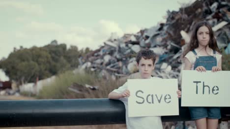 Save-the-planet.-young-kids-holding-signs-standing-in-a-large-junkyard