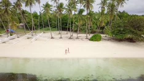 Drone-shot-aerial-view-of-young-couple-walking-on-tropical-beach-in-the-Philippines.-Palm-trees-and-clear-blue-water.-People-travel-love-romance-vacations-concept.-4K-resolution-video