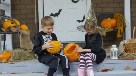 Kleinen-Bruder-und-Schwester-in-Halloween-Kostümen-spielen-mit-Kürbissen