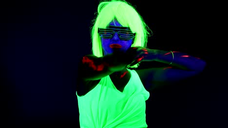 Woman-with-UV-face-paint,-wig,-glowing-clothing-dancing-in-front-of-camera.-Caucasian-woman.-.