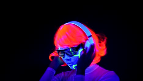 Woman-with-UV-cyborg-face-paint,-wig,-glowing-glasses,-clothing-dancing-and-listening-to-music-with-headphones.-Asian-woman.-.