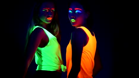 Women-with-UV-face-paint,-glowing-bracelets,-glowing-clothing-dancing-together-in-front-of-camera,-Half-body-shot.-Caucasian-and-asian-woman.-.