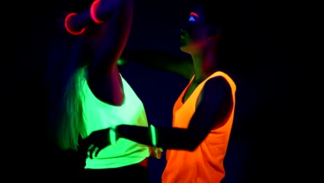 Women-with-UV-face-paint,-glowing-bracelets,-glowing-clothing-dancing-together-in-front-of-camera,-Half-body-shot.-Caucasian-and-asian-woman.-.