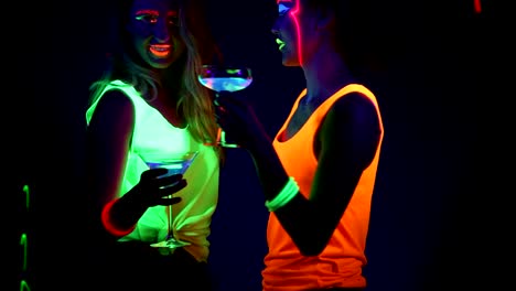 Women-with-UV-face-paint,-laser,-glowing-bracelets,-drinks,-glowing-clothing-dancing-together-in-front-of-camera,-tilt-up-shot.-Caucasian-and-asian-woman.-.