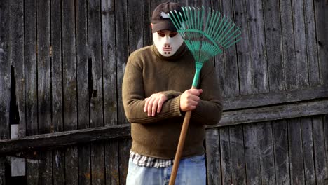 Man-in-a-Halloween-mask-with-a-rake-at-the-old-barn-wall