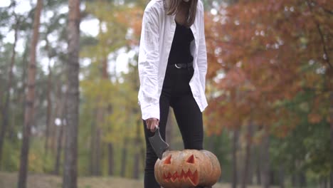 Halloween.-Girl-with-a-butcher's-knife-coming-to-a-pumpkin