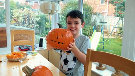 Young-boy-smiling-to-camera-holding-up-a-Jack-O-Lantern-for-Halloween