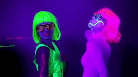 Langsame-Motin-von-schönen-sexy-Frauen-mit-fluoreszierenden-Make-up-und-Kleidung-Tanz-im-Neonlicht.-Night-Club,-Party-Konzept.