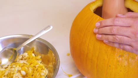 Hombre-cucharadas-de-semillas-de-una-calabaza-grande-de-naranja-y-gotas-les-en-un-recipiente-de-Metal