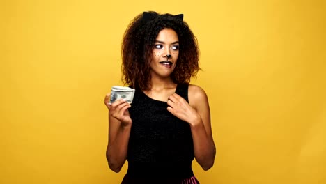Young-african-tricky-woman-counting-cash-and-hiding-money-isolated-over-yellow-background