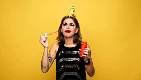 Upset-crying-woman-with-halloween-make-up-and-holiday-cap-has-problem-with-blowing-soap-bubbles-isolated-over-yellow