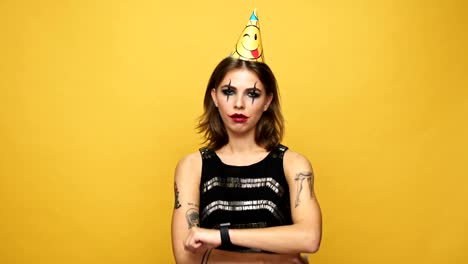 Unhappy-creepy-lady-with-dark-make-up-and-cap-blowing-birthday-horn-isolated-over-yellow