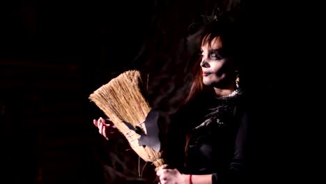 Halloween-party,-night,-frightening-portrait-of-a-woman-in-the-twilight,-in-the-rays-of-light.-woman-with-a-terrible-make-up-in-a-black-witch-costume.-she-holds-a-broom-with-a-bat