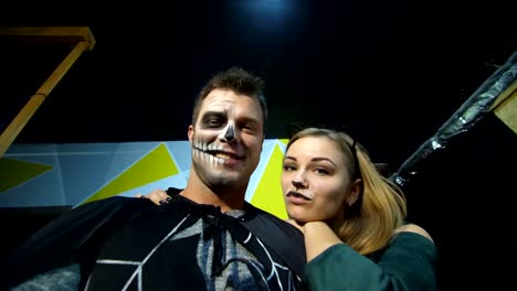 Halloween-party,-night,-frightening-portrait-of-a-man-with-a-terrible-makeup-in-a-black-costume-and-a-girl-in-a-cat-costume,-they-croak-in-front-of-the-camera