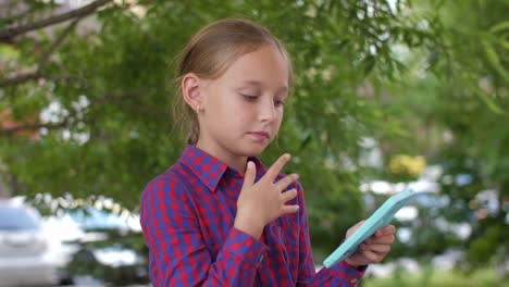 Blonde-young-girl-using-cell-phone-and-waving-insects-away-in-green-park