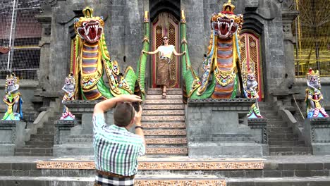 Ein-Mann-nimmt-Bilder-einer-Frau-auf-einem-Smartphone-vor-dem-Eingang-zu-einem-buddhistischen-Tempel