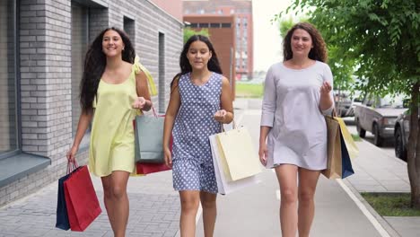 Three-beautiful-girls-walk-down-the-street-after-shopping.-4K