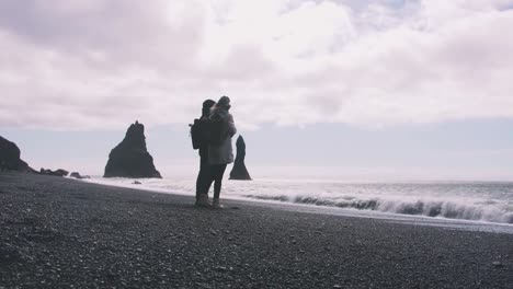 Young-couple-holding-hands-on-black-sand-beach-in-Iceland,-slow-motion
