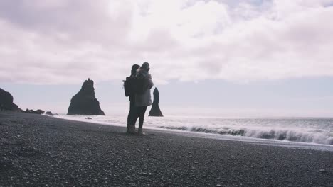 Joven-pareja-cogidos-de-la-mano-en-la-playa-de-arena-negra-en-Islandia,-cámara-lenta