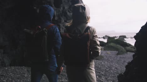 Young-couple-holding-hands-walking-down-black-sand-beach-in-Iceland,-slow-motion
