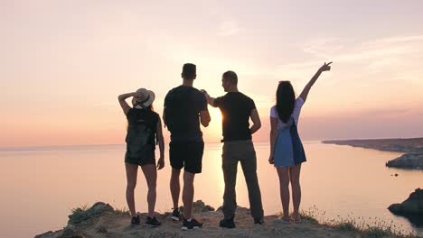 Back-view-group-of-young-friends-enjoying-raising-hands-up-and-talking-about-magnificent-sunset