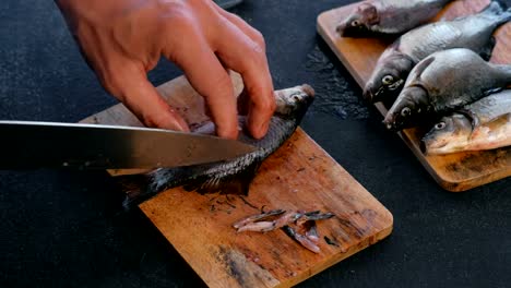 Man-cuts-the-fins-of-the-carp-fish-on-wooden-board.-Cooking-fish.-Hands-close-up.