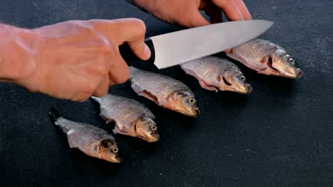 Man-makes-cuts-on-carp-fish-on-black-table.-Cooking-fish.-Close-up-hand.