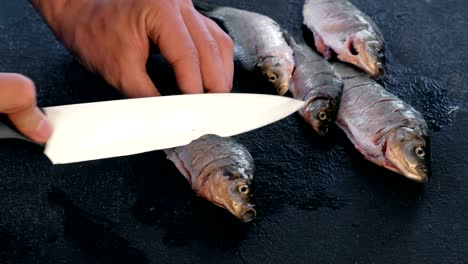 Man-makes-cuts-on-carp-fish-on-black-table.-Cooking-fish.-Close-up-hand.