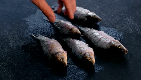 Man-turns-the-carps-fish-on-the-table-and-sprinkles-it-with-spices.-Cooking-fish.-Hand-close-up.