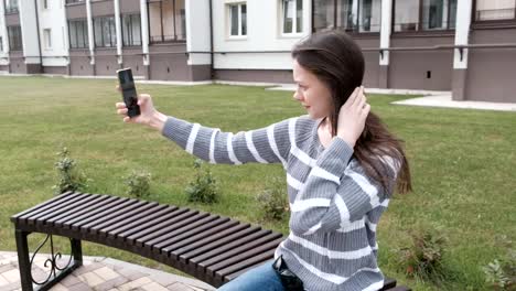 Preciosa-morena-está-intentando-tomar-un-selfie-en-su-teléfono-móvil-en-el-viento-mientras-está-sentado-en-el-Banco.