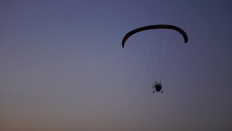 Der-Pilot-auf-einem-Gleitschirm-fliegt-von-der-Kamera-allmählich-Weg-in-die-Ferne-gegen-den-Sonnenuntergang-schönen-Himmel.-Schöner-Hintergrund-Hintergrundbild.-Begriff-der-Freiheit