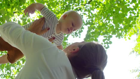 Glückliche-Mutter-heben-und-küssen-Baby-im-Park