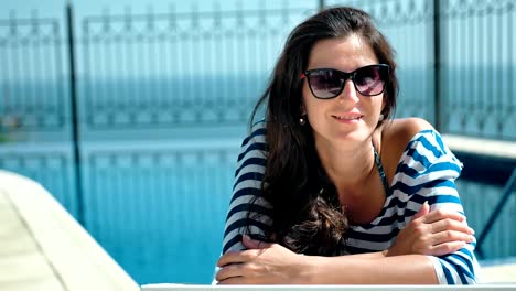 Portrait-happy-smiling-woman-in-sunglasses-enjoying-vacation-lying-on-deck-chair-with-arms-crossed