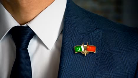 Geschäftsmann-zu-Fuß-in-Richtung-Kamera-mit-Freund-Land-Flaggen-Pin-Pakistan---China