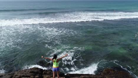 Young-woman-open-arms-on-cliff-edge-at-seaside,aerial-drone-4k-footage