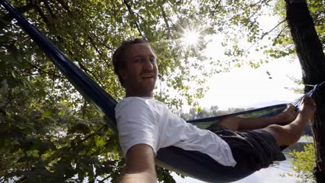 Joven-toma-selfie-en-hamaca-relajante-por-el-río-en-verano