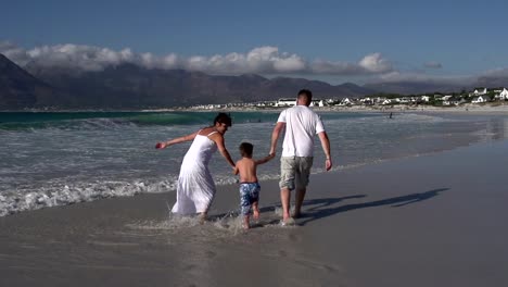 Slow-motion-of-couple-swinging-child-through-waves,-South-Africa