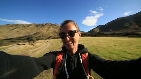 Young-female-hiking-takes-selfie-portrait-with-mountains-on-background