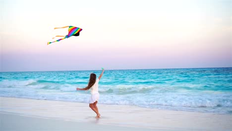 Little-girl-with-flying-kite-on-tropical-beach.-Kid-play-on-ocean-shore.-Child-with-beach-toys-in-slow-motion