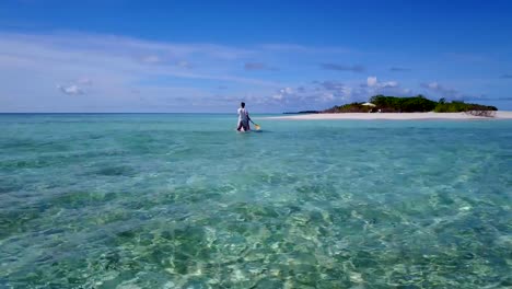 v03861-vuelo-drone-vista-aérea-de-Maldivas-playa-2-personas-pareja-hombre-mujer-relajante-en-paddleboard-en-isla-paraíso-soleado-con-cielo-azul-aqua-agua-mar-4k