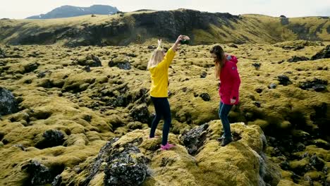 Aerial-view-of-two-woman-standing-on-the-rock,-looking-on-the-lava-field-in-Iceland-and-dancing,-feeling-freedom,-happy