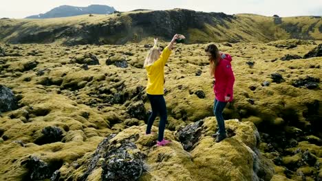 Vista-aérea-de-dos-mujer-de-pie-sobre-la-roca,-mirando-en-el-campo-de-lava-en-Islandia-y-el-baile,-esta-libertad,-feliz