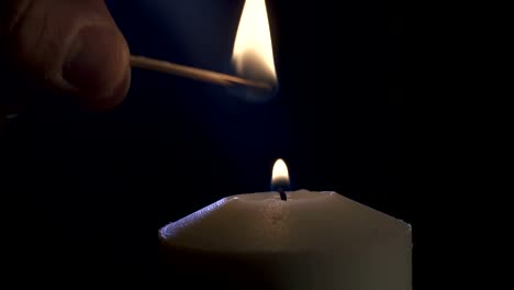 Slow-motion-macro-footage-of-a-white-candle-lit-by-a-match-on-a-dark-background