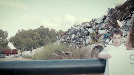 Save-the-planet.-young-kids-holding-signs-standing-in-a-junkyard